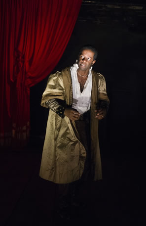 Aldridge playing Othello in gold cloak, ruffled shirt and black pants with a red velvet curtain pulled back behined his right shoulder